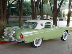 an old green and white car parked in front of some trees