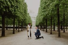 a man and woman are kissing in the middle of a tree lined road with trees lining both sides