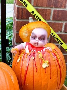 a baby in a pumpkin costume sitting next to two large pumpkins with blood on them