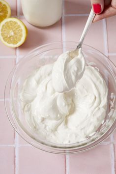 a person is spooning cream into a glass bowl with lemons and milk in the background