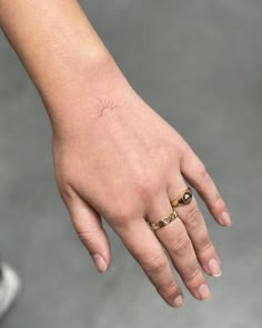 a person's hand with a small sun tattoo on their left wrist and ring