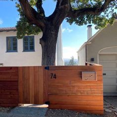 a wooden fence in front of a house with a large tree on the side of it