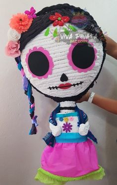 a doll made to look like a skeleton with flowers in her hair, wearing a pink and blue dress