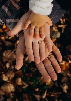 two hands holding each other with wedding rings on their fingers in front of some leaves