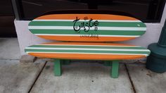 an orange and white surfboard sitting on top of a green bench