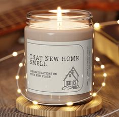 a candle is sitting on a table with some lights around it that says, that new home smell