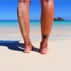 a person standing on the beach with their feet in the sand and palm tree tattoo