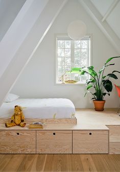 an attic bedroom with white walls and wood flooring is furnished with a bed, nightstands, potted plant and stuffed animal