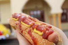 a hand holding a hot dog with mustard and ketchup on it's bun