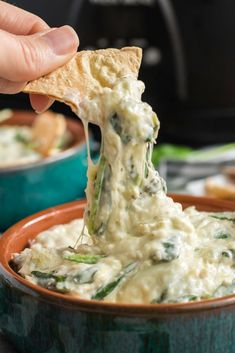 a hand dipping a tortilla chip into a bowl of dip