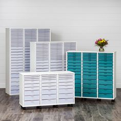 three white and blue storage cabinets sitting on top of a hard wood floor next to a vase with flowers