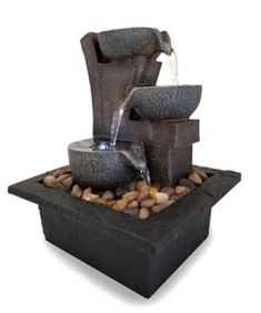 an outdoor fountain with rocks and water pouring out of it's sides, on top of a black stone slab