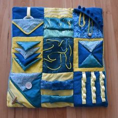 a blue and yellow patchwork quilt with buttons on it's side, hanging from a hook