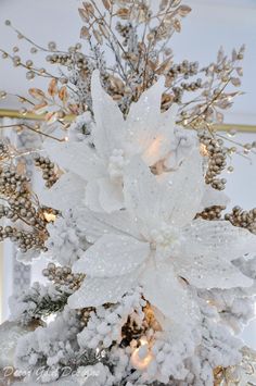 a white and gold christmas tree decorated with frosted branches, lights and flowers in the center