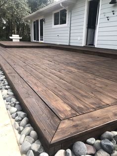 a wooden deck in front of a house with rocks on the ground and gravel around it