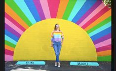 a woman standing in front of a colorful wall with the word shine painted on it