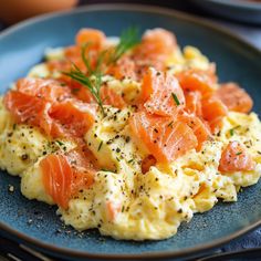 a blue plate topped with scrambled eggs and smoked salmon slices, garnished with herbs