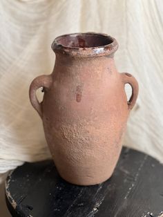 a brown vase sitting on top of a wooden table next to a white cloth covered wall