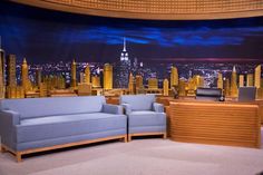 the late show set with two couches and a chair in front of a cityscape