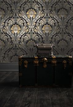 an old fashioned typewriter sitting on top of a trunk in front of a wallpapered background