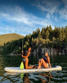 two women sitting on a paddle board in the water