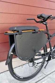 a bicycle parked next to a red wall with a black bag on it's back