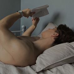 a naked man laying in bed reading a book