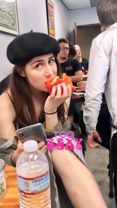 a woman sitting at a table eating food with her legs crossed and wearing a hat