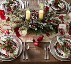 the table is set for christmas dinner with silverware and red berries, pine cones, greenery