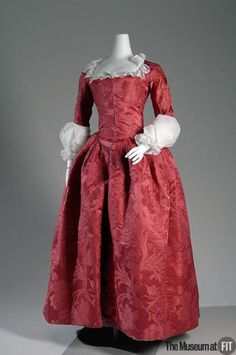 a red dress with white ruffles on the collar and sleeves is displayed in front of a gray background