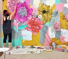 a woman is painting flowers on a wall