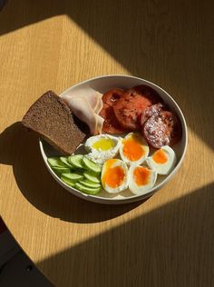 a white bowl filled with eggs, meat and veggies on top of a wooden table