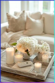 a tray with candles, flowers and remotes sitting on a table in front of a couch