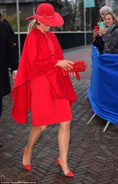 a woman in a red dress and hat walking down the street