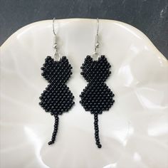 Share your love of cats with these adorable black cat beaded earrings. These simple but stylish earrings are made with brick stitch pattern with a single dangling tail. Please note the bottom of tail may curl different ways.  If you are looking for other colored cats - please see alternate listings  https://www.etsy.com/shop/whiskerswingsdesigns/?etsrc=sdt&section_id=48258463 Message me for custom options! As a fellow cat lover, I would love to find the right pair for you and your cats! Details: Black Cat Bead Pattern, Cat Seed Bead Patterns, Beaded Black Cat Earrings, Bead Cat Earrings, Beaded Cat Earrings, Halloween Earrings Beaded, Beaded Cat, Cats Orange, Cat Earring