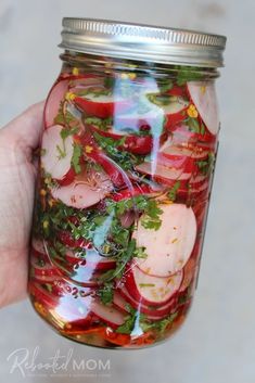 a hand holding a mason jar filled with pickled radishes and other veggies