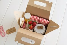 an open cardboard box filled with food on top of a white wooden floor next to a red and white checkered ribbon