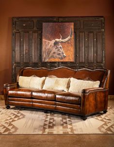 a brown leather couch sitting in front of a wooden wall with an animal painting on it