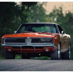 an orange muscle car parked on the side of the road with trees in the background