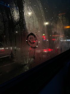 the rain is pouring down on a window with a smiley face sticker in it