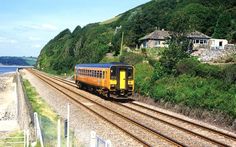 a train traveling down tracks next to a lush green hillside