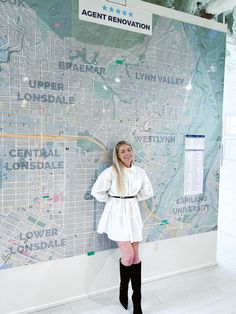 a woman standing in front of a map with her hands on her hips and wearing black over the knee boots