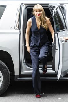 the woman is stepping out of the car with her foot in the open door and wearing red shoes