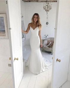 a woman in a white wedding dress is standing by the door and looking into the mirror