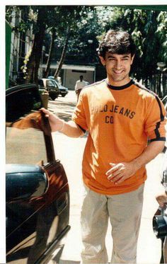 a man in an orange shirt standing next to a car