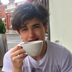 a young man drinking out of a white cup