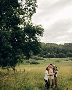 a man and woman are standing in the middle of a field with trees behind them