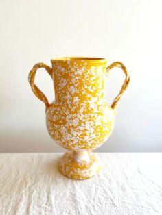 a yellow and white vase sitting on top of a table next to a white wall