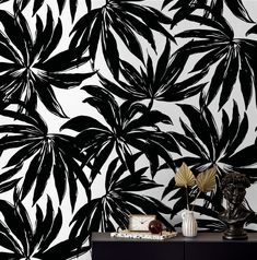 a black and white wallpaper with large leaves on the sideboard next to a vase