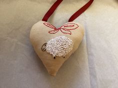 a heart shaped ornament with a sheep on it's side hanging from a red ribbon